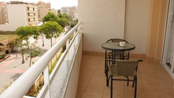 A balcony with a table and chairs, overlooking a street with trees and buildings.