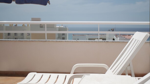 Un balcone con sedie in plastica bianca e un ombrellone blu, con vista sulla città costiera.