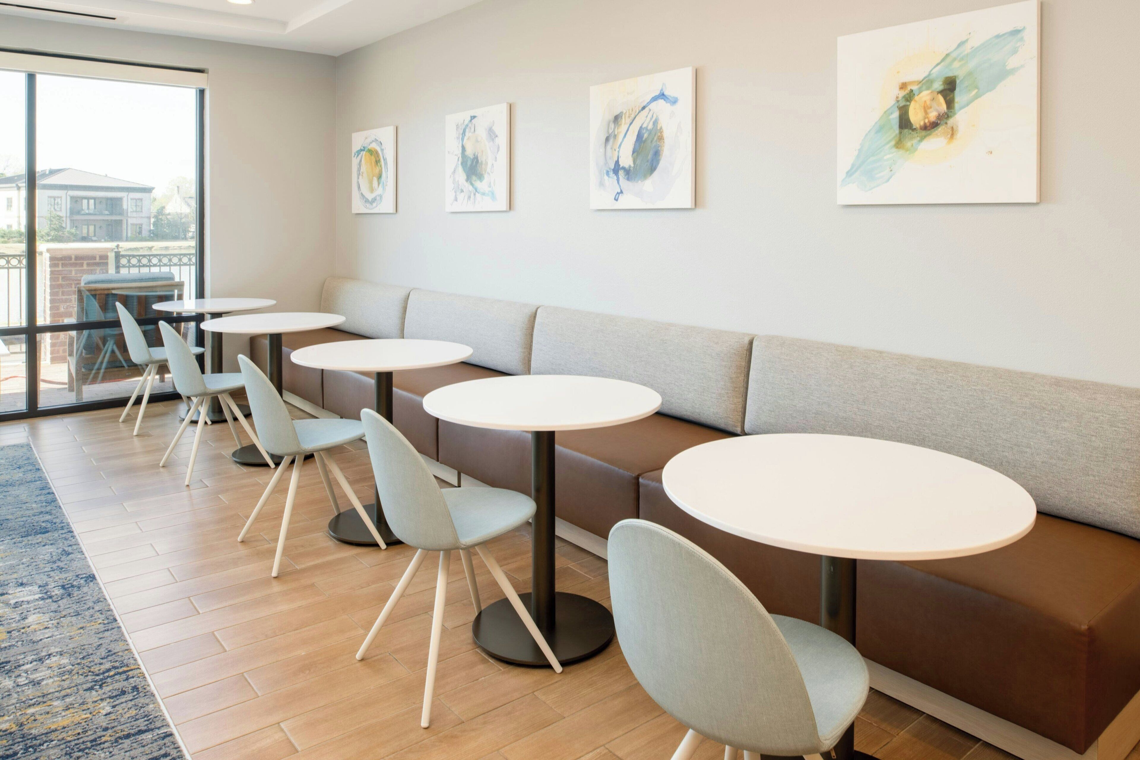 A modern interior with a long bench, multiple round tables, and chairs.