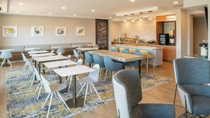A modern dining area with tables and chairs, a kitchen area, and a seating area with a wall-mounted artwork. - TownePlace Suites Jackson Ridgeland/Township at Colony Park (Ridgeland)