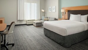 A hotel room with a large bed, a desk, a chair, a small sofa, and a window with curtains. - TownePlace Suites Jackson Ridgeland/Township at Colony Park (Ridgeland)