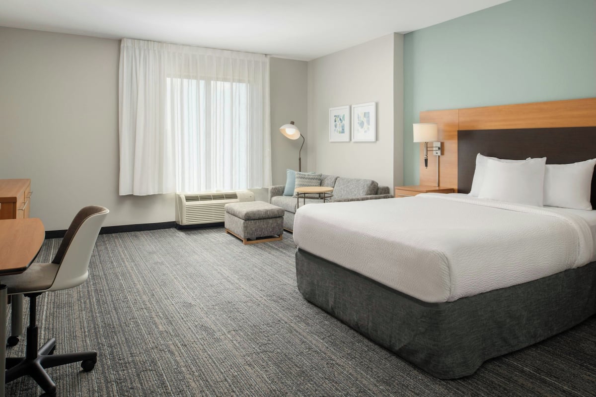 A hotel room with a large bed, a desk, a chair, a small sofa, and a window with curtains.