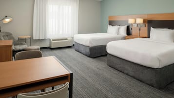 A hotel room with two beds, a desk, a chair, a lamp, and a window with curtains.