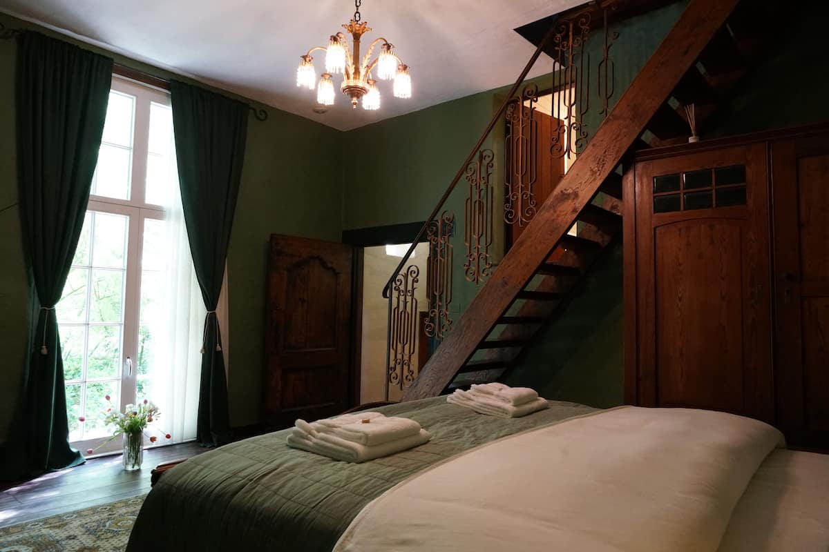 A bedroom with a large bed, a wooden staircase, and a chandelier.
