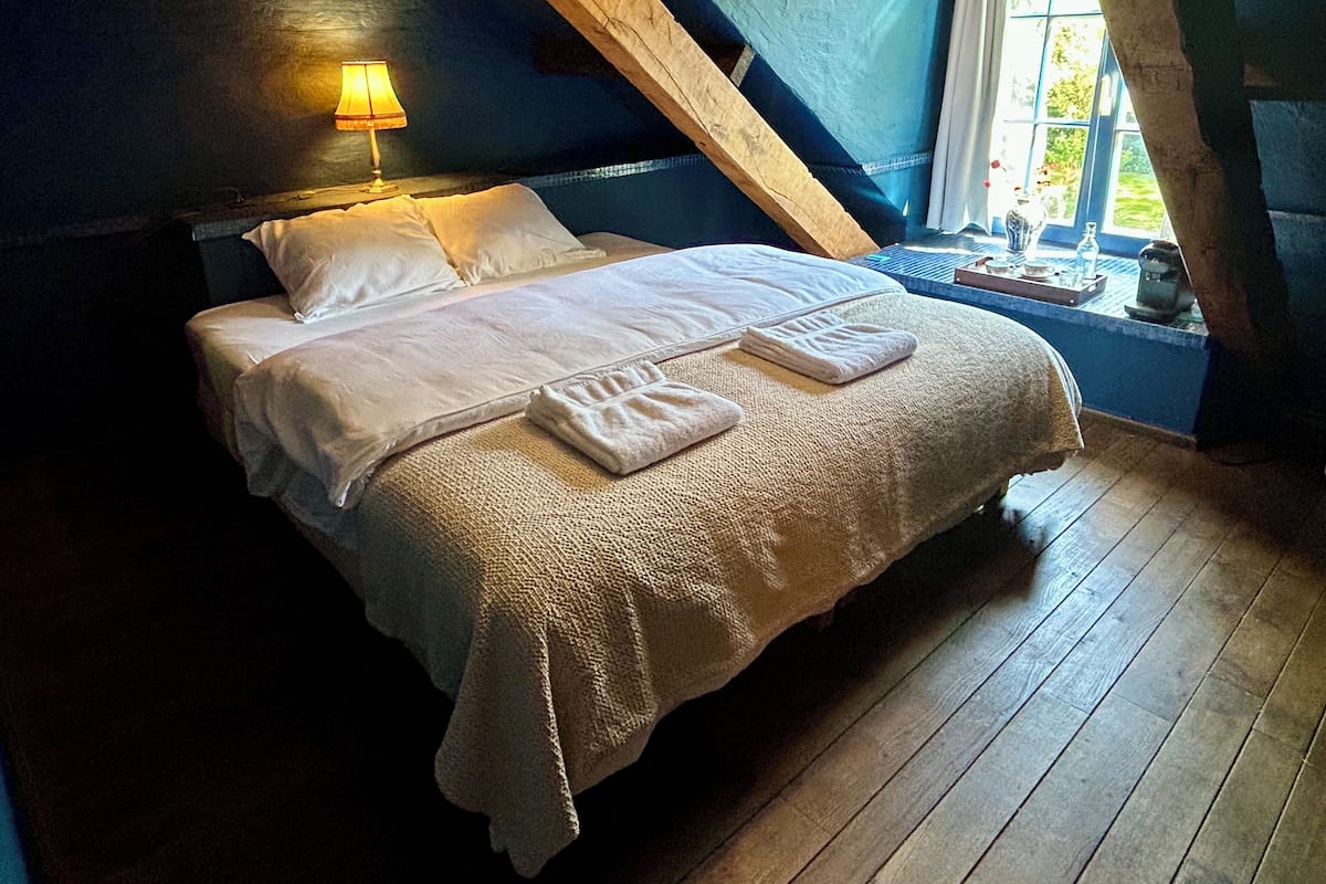 A bedroom with a bed, pillows, a lamp, and a window.