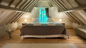 A cozy attic bedroom with a sloped ceiling, a large bed with pillows, bedside lamps, and a view through a window. - B&B Pronkenburg (Bruges)