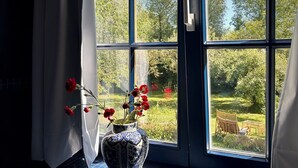 A window with a view of a garden, a vase with flowers, and a chair outside. - B&B Pronkenburg (Bruges)