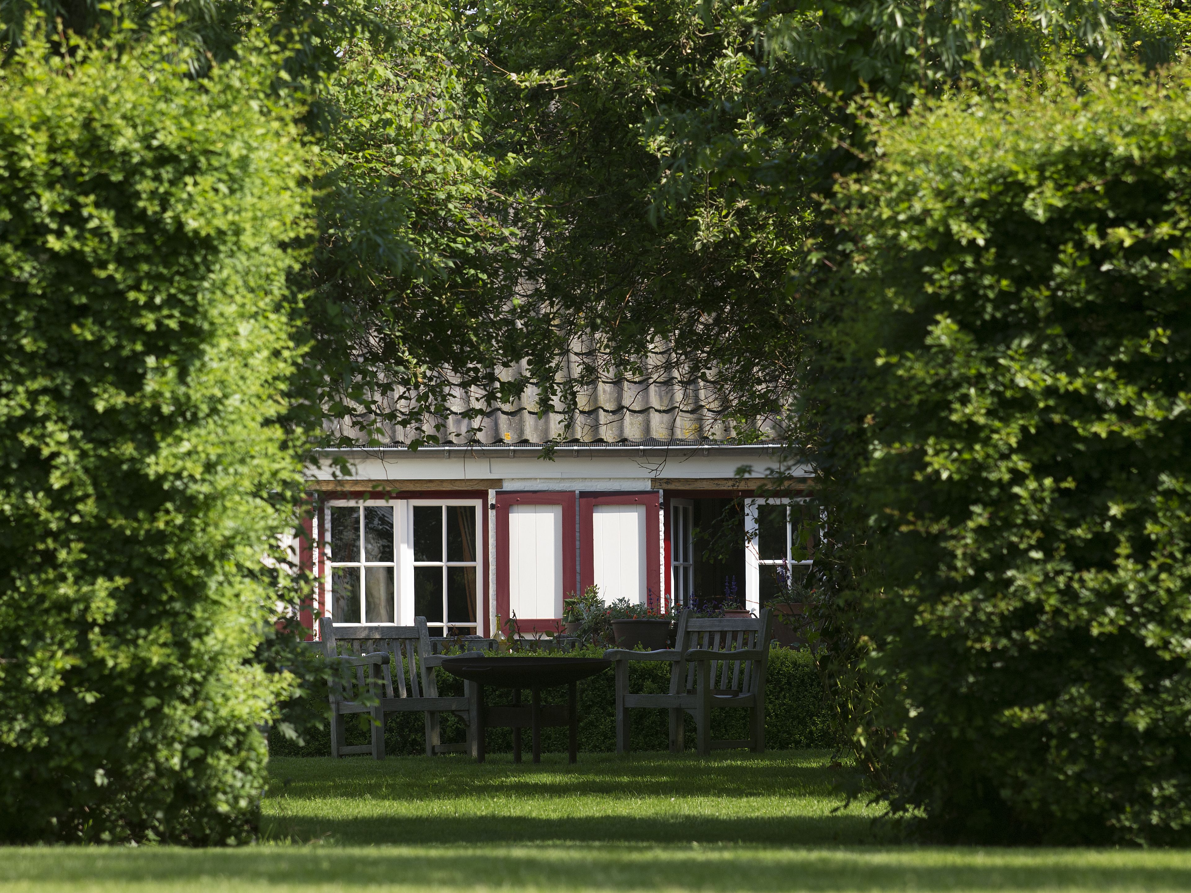 A house with a red door and white shutters, surrounded by lush green trees.