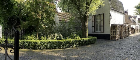 Une rue pavée bordée d’arbres et un bâtiment blanc avec un toit recouvert de tuiles.