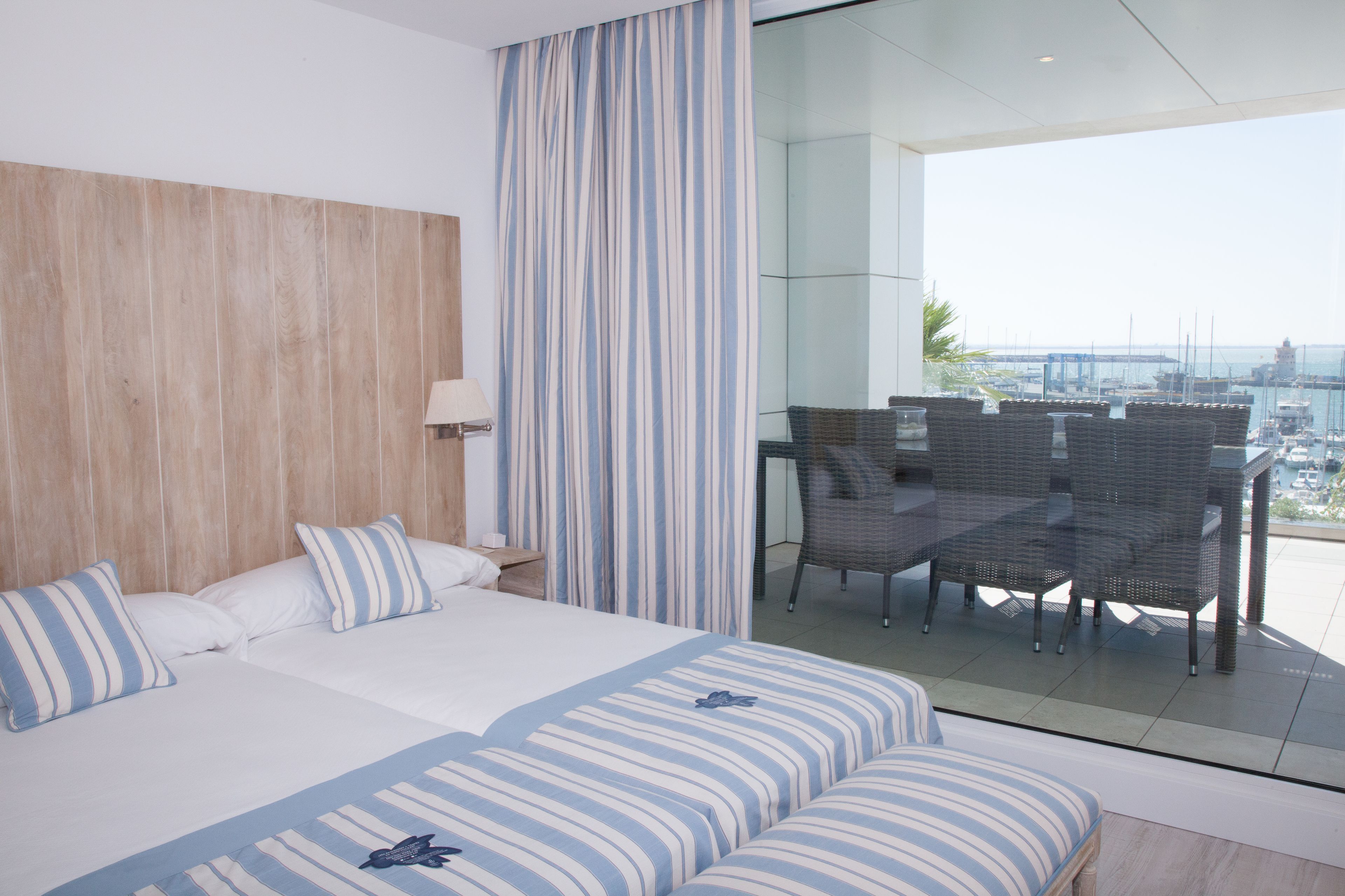 Ein Hotelzimmer mit einem großen Bett, einem Balkon mit Korbmöbeln und Blick auf den Yachthafen.