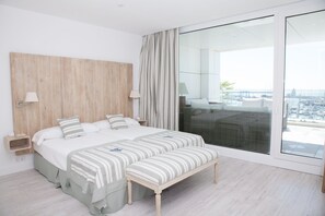 A modern bedroom with a large bed, a bench, and a view of the city through a balcony. - Las Suites de Puerto Sherry (El Puerto de Santa Maria)
