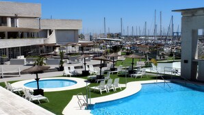 A swimming pool with lounge chairs and umbrellas, surrounded by a marina with boats. - Las Suites de Puerto Sherry (El Puerto de Santa Maria)