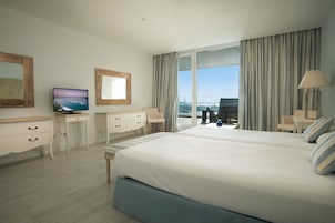 A hotel room with a large bed, a TV, a desk, and a view of the city.