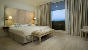 A hotel room with a large bed, a bench, a nightstand, a lamp, and a view of the sea through a sliding glass door. - Las Suites de Puerto Sherry (El Puerto de Santa Maria)