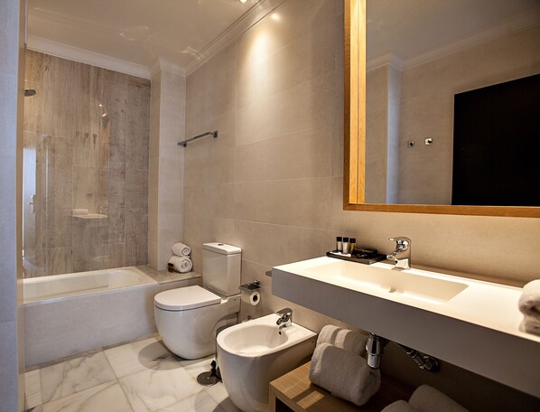 Un baño moderno con bañera, inodoro, bidé y un espejo grande.