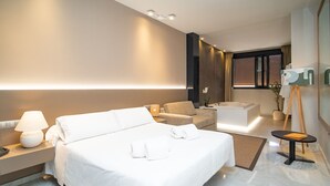 A modern hotel room with a large bed, a sitting area, a bathtub, and a small table with a lamp. - Hotel Barrameda (Sanlucar de Barrameda)