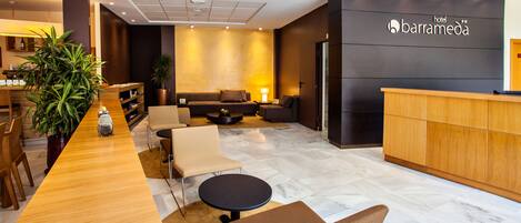 Een hotel lobby met een receptiebalie, een zithoek en een grote potplant.