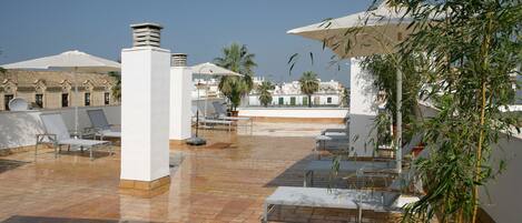 A rooftop terrace with lounge chairs, umbrellas, and a potted plant.