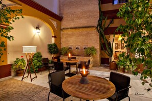 Un patio al aire libre con mesas y sillas de madera redondas, plantas en macetas y una pared de ladrillo.