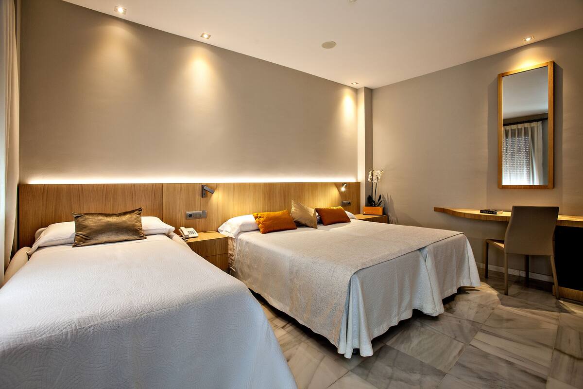 A hotel room with two beds, a desk, and a chair.