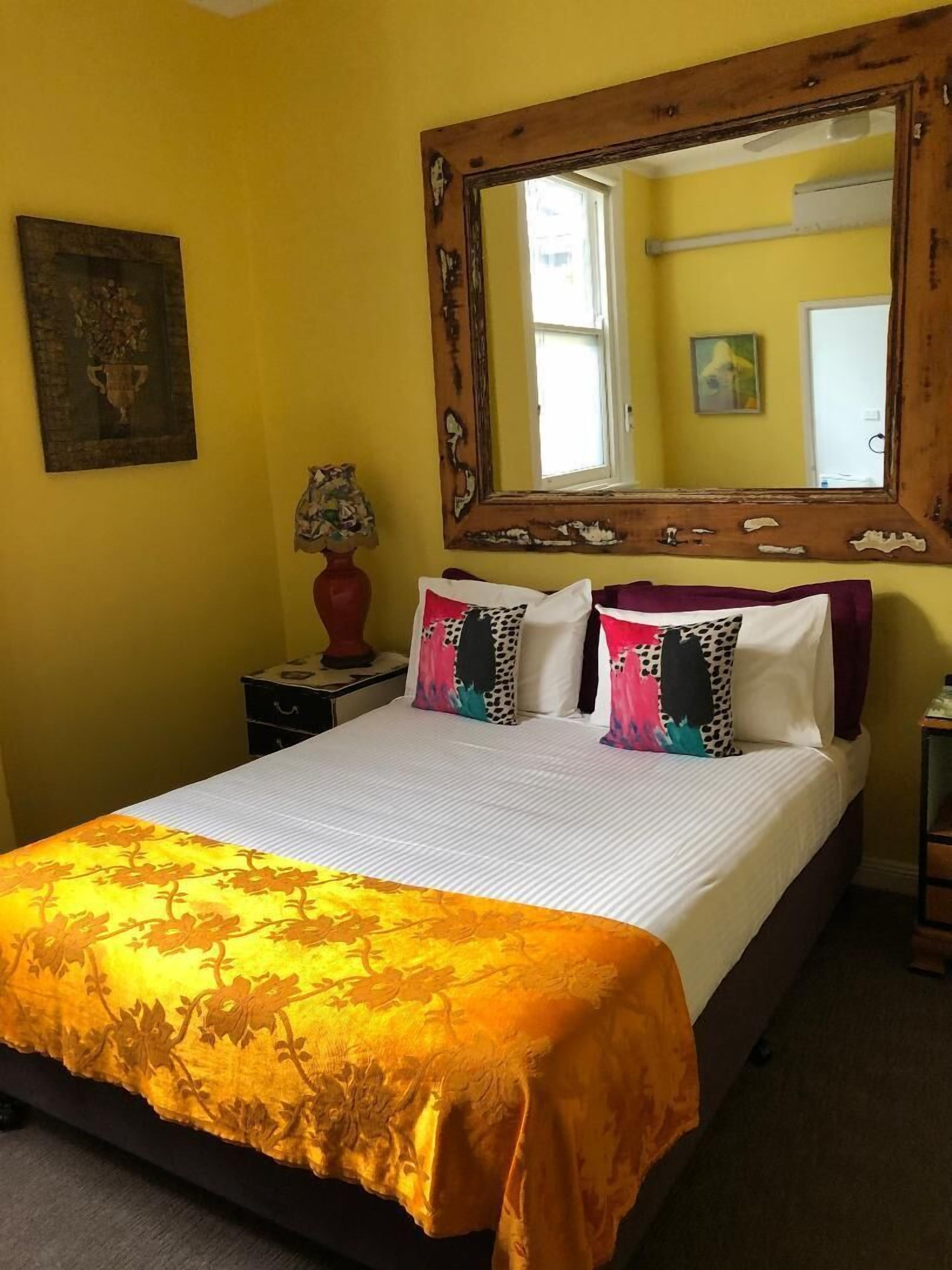 A bed with a floral bedspread, a mirror above it, and a lamp on a bedside table.