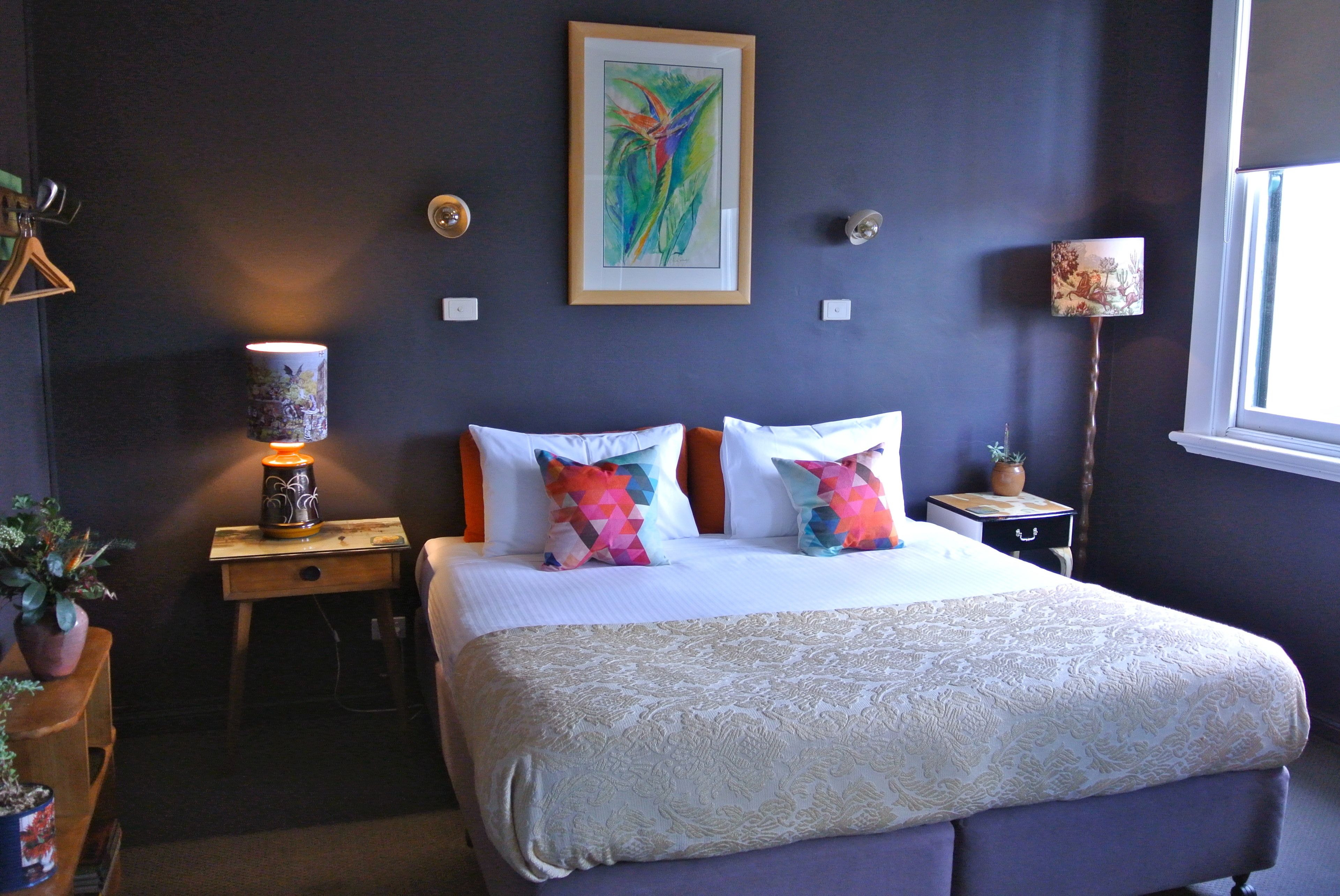 A neatly arranged bedroom with a bed, pillows, a bedside table with a lamp, a small nightstand, and a window.