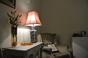 A room with a table, a lamp, a chair, and a refrigerator.
