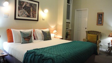Una cama bien tendida con un edredón verde, varios almohadones y una obra de arte enmarcada encima.