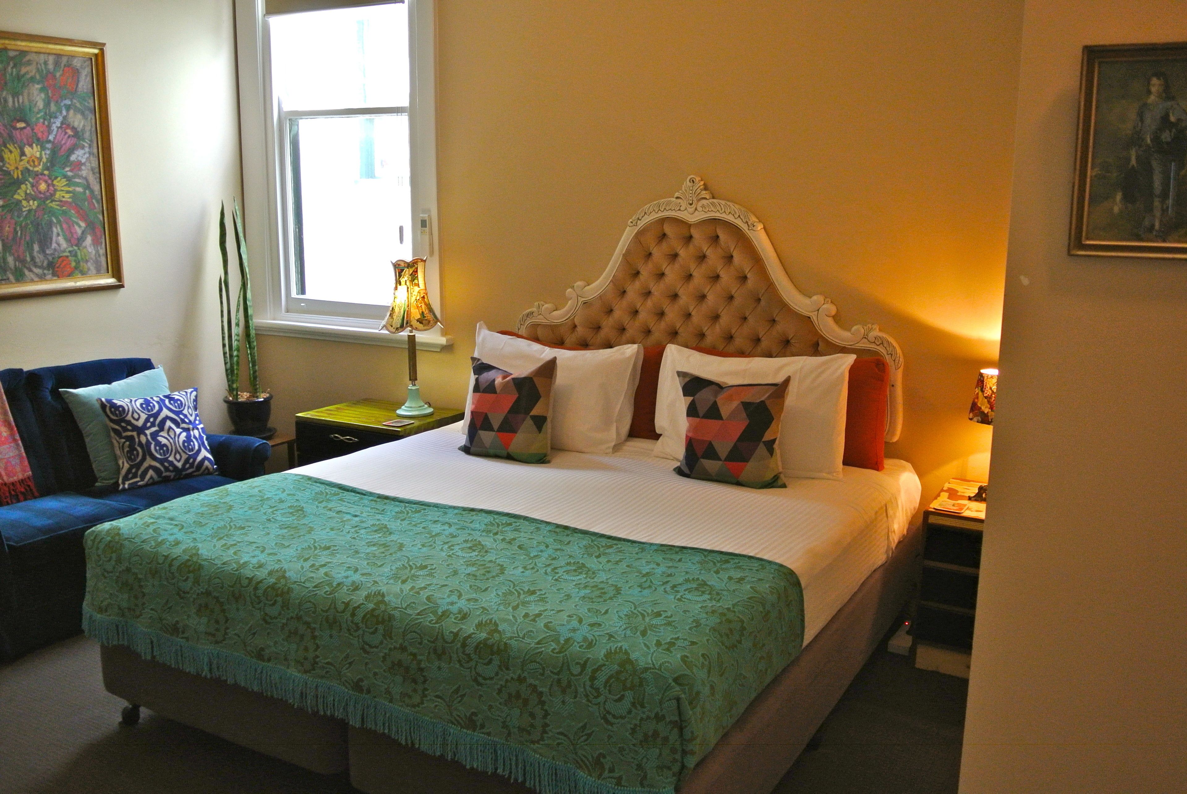 A neatly made bed with patterned pillows, a green bedspread, and a decorative headboard.