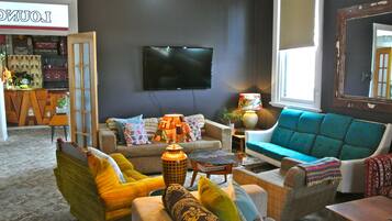 A living room with a sofa, armchairs, and a television. There is a window with a view of the outside.