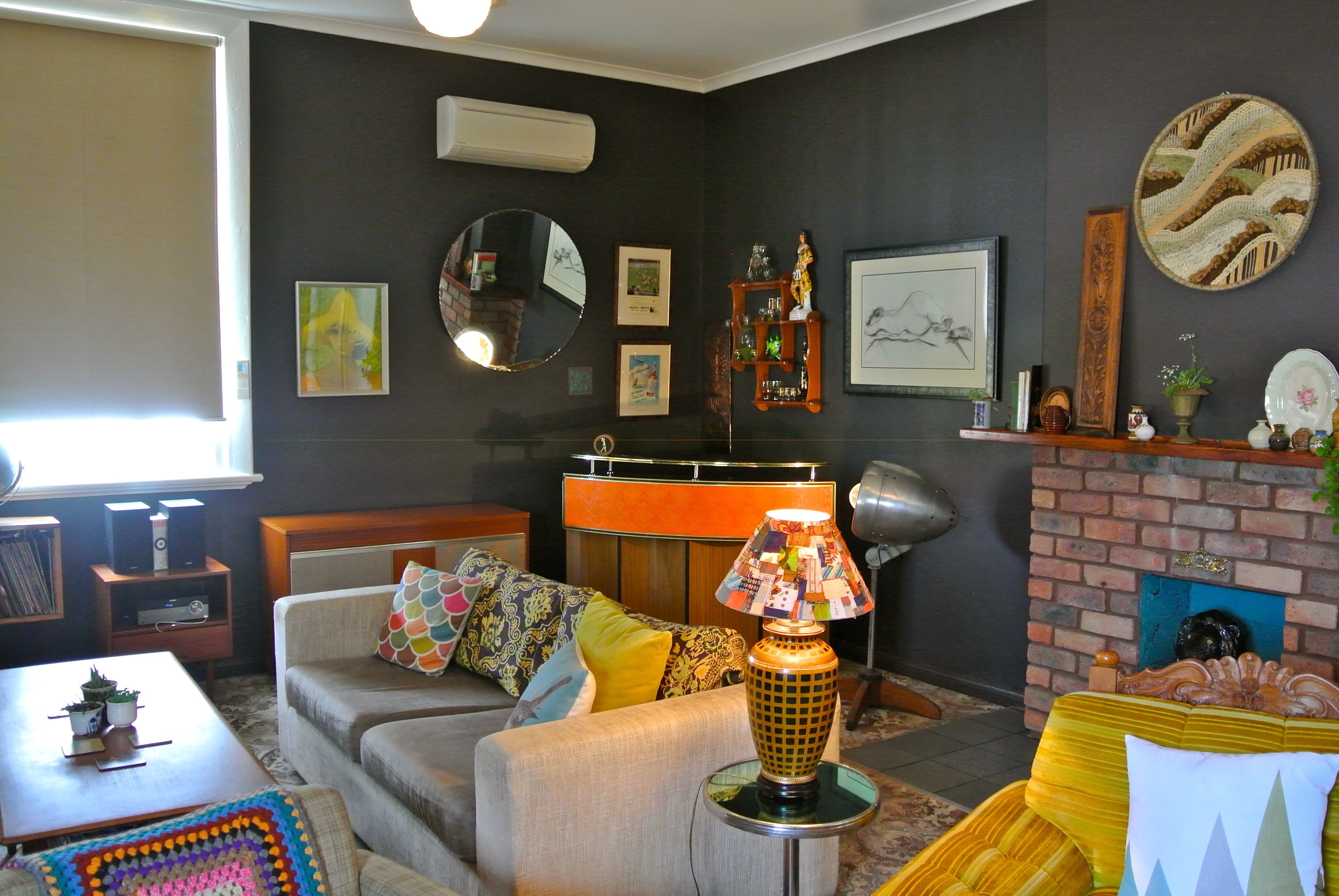 A living room with a sofa, coffee table, and a lamp. There are framed pictures on the wall and a fireplace.