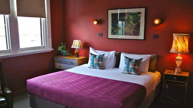 A bedroom with a bed, two bedside tables, a window, and a wall-mounted picture. - Vine Valley Inn (Cessnock)