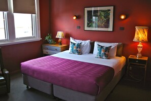 Un dormitorio con cama, dos mesitas de noche, una ventana y un cuadro colgado en la pared.