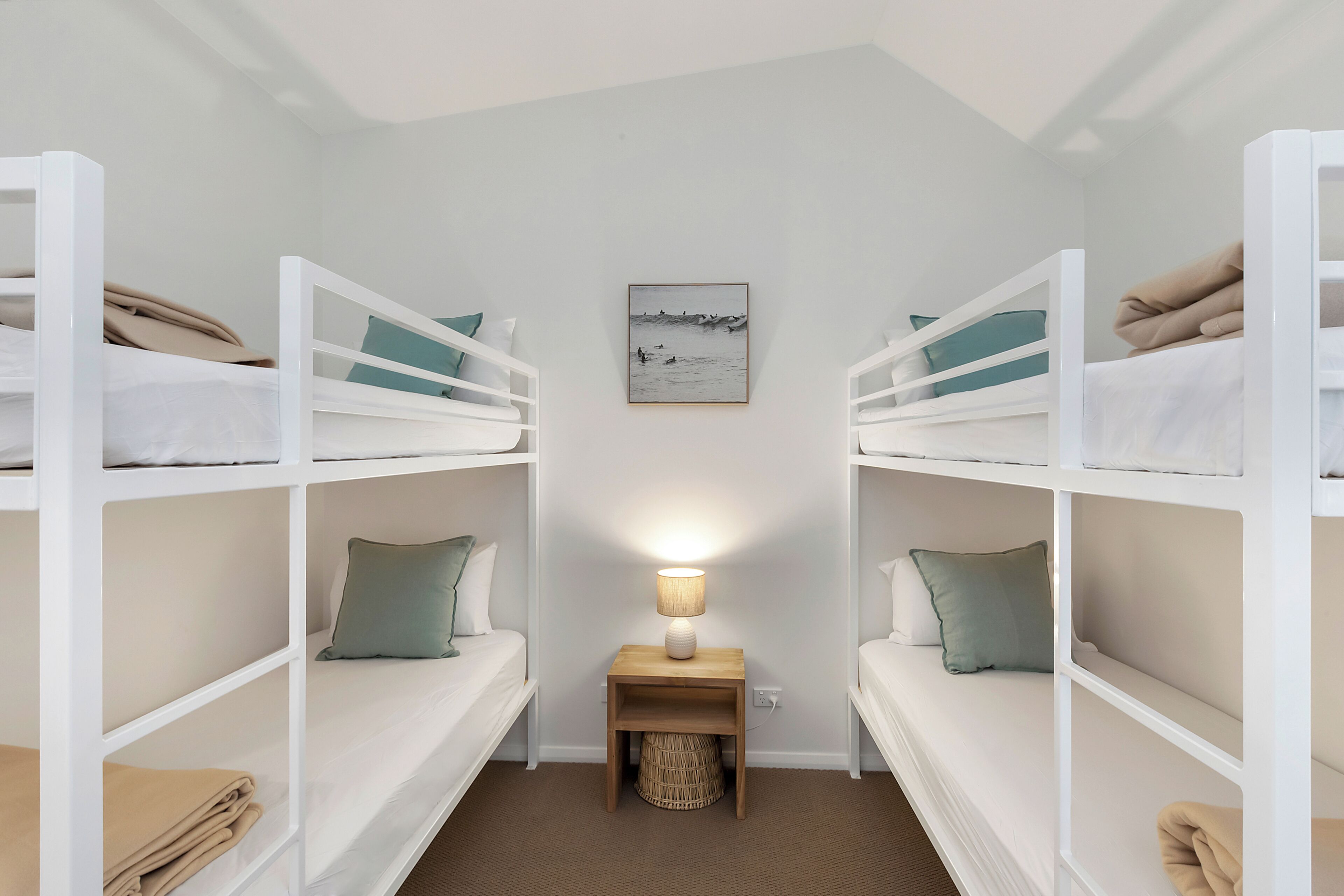 Une chambre avec un lit superposé, une table de chevet et une lampe, un tableau encadré au mur et un panier en osier placé sous la table de chevet.