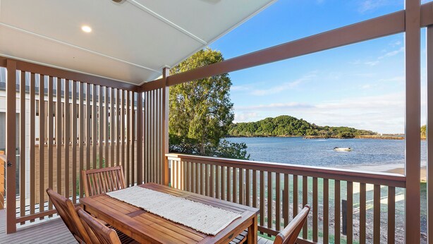 A wooden deck with a table and chairs, overlooking a body of water and a distant shoreline. - Reflections Massy Greene - Holiday Park (Brunswick Heads)