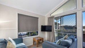 A modern living room with a large window, a flat-screen TV, and a sofa set. - Reflections Massy Greene - Holiday Park (Brunswick Heads)