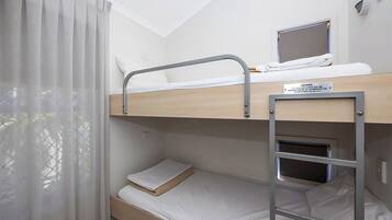 Un lit superposé avec un ordinateur portable posé sur le lit du haut, une petite fenêtre et un panneau d’avertissement indiquant la hauteur du lit.