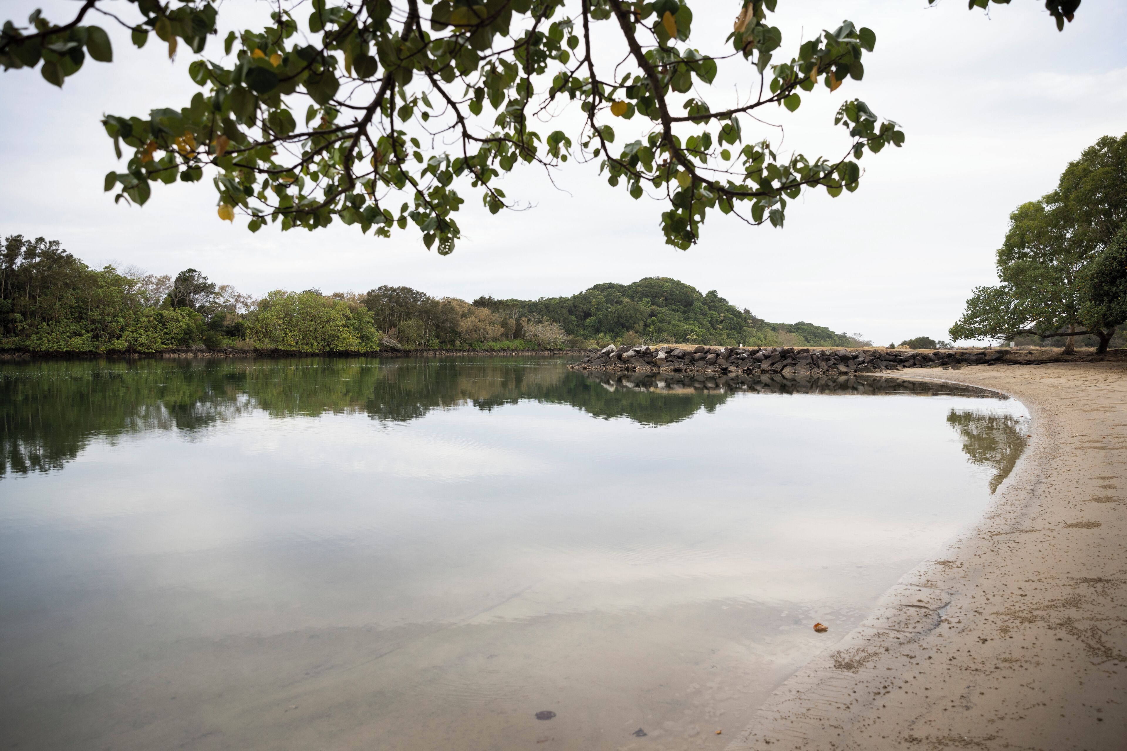 A calm river with a sandy bank and trees in the background.