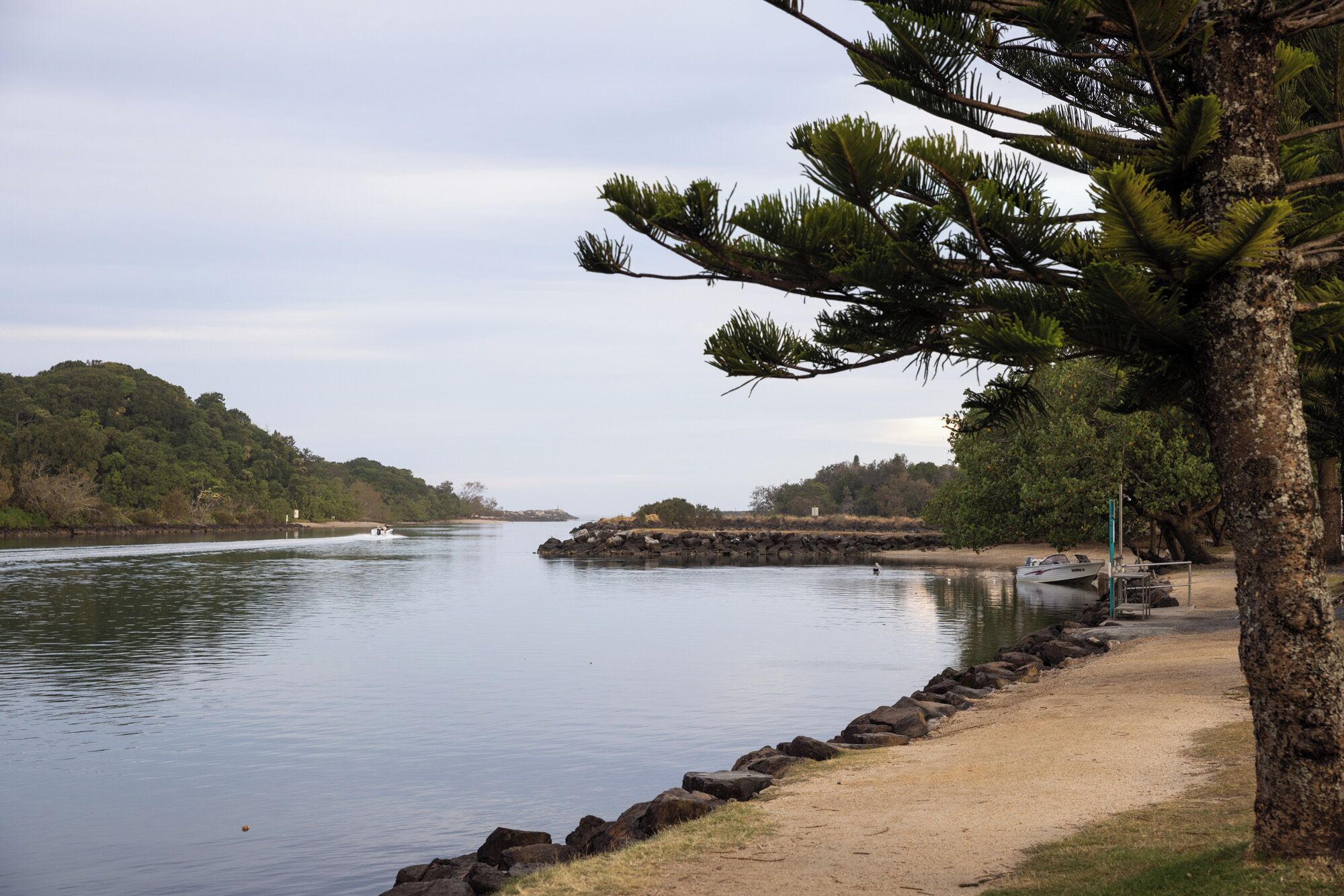 A calm lake with a sandy beach, a rocky outcrop, and a boat docked on the shore.