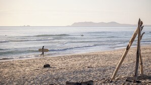 A beach with a surfboard, a wooden structure, and distant mountains. - Reflections Massy Greene - Holiday Park (Brunswick Heads)