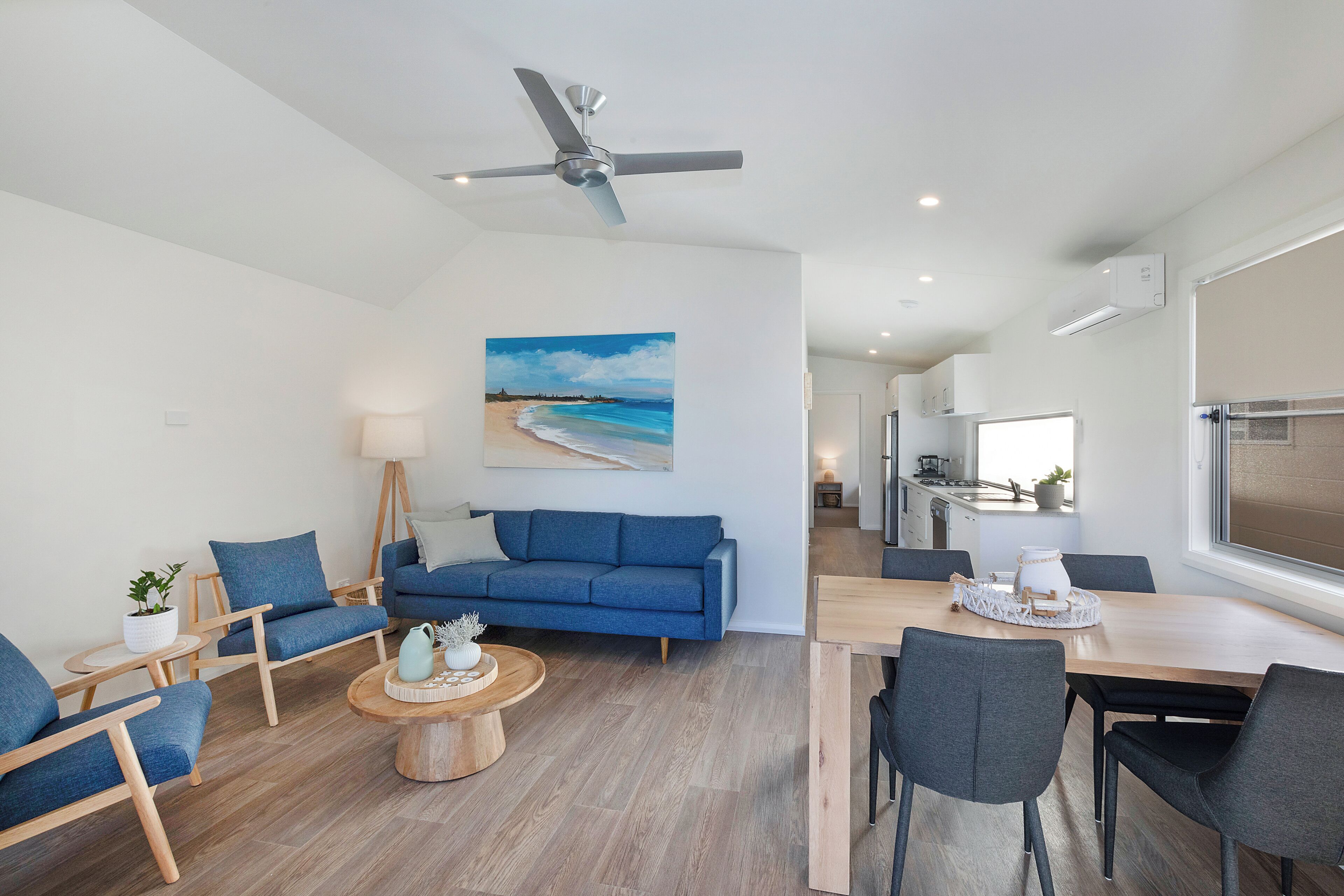 A modern living room with a blue sofa, wooden coffee table, and a dining area with a wooden table and chairs.