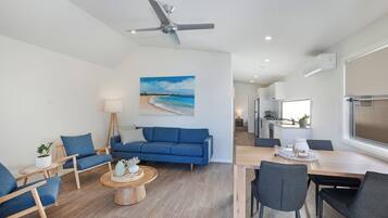 A modern living room with a blue sofa, wooden coffee table, and a dining area with a wooden table and chairs.