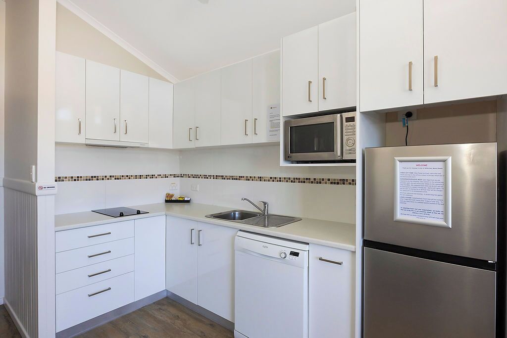 A modern kitchen with white cabinets, a stainless steel refrigerator, a microwave, and a dishwasher.