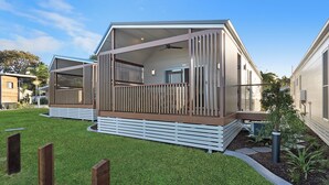 A modern, two-story mobile home with a balcony, surrounded by well-maintained grass and a small garden. - Reflections Massy Greene - Holiday Park (Brunswick Heads)
