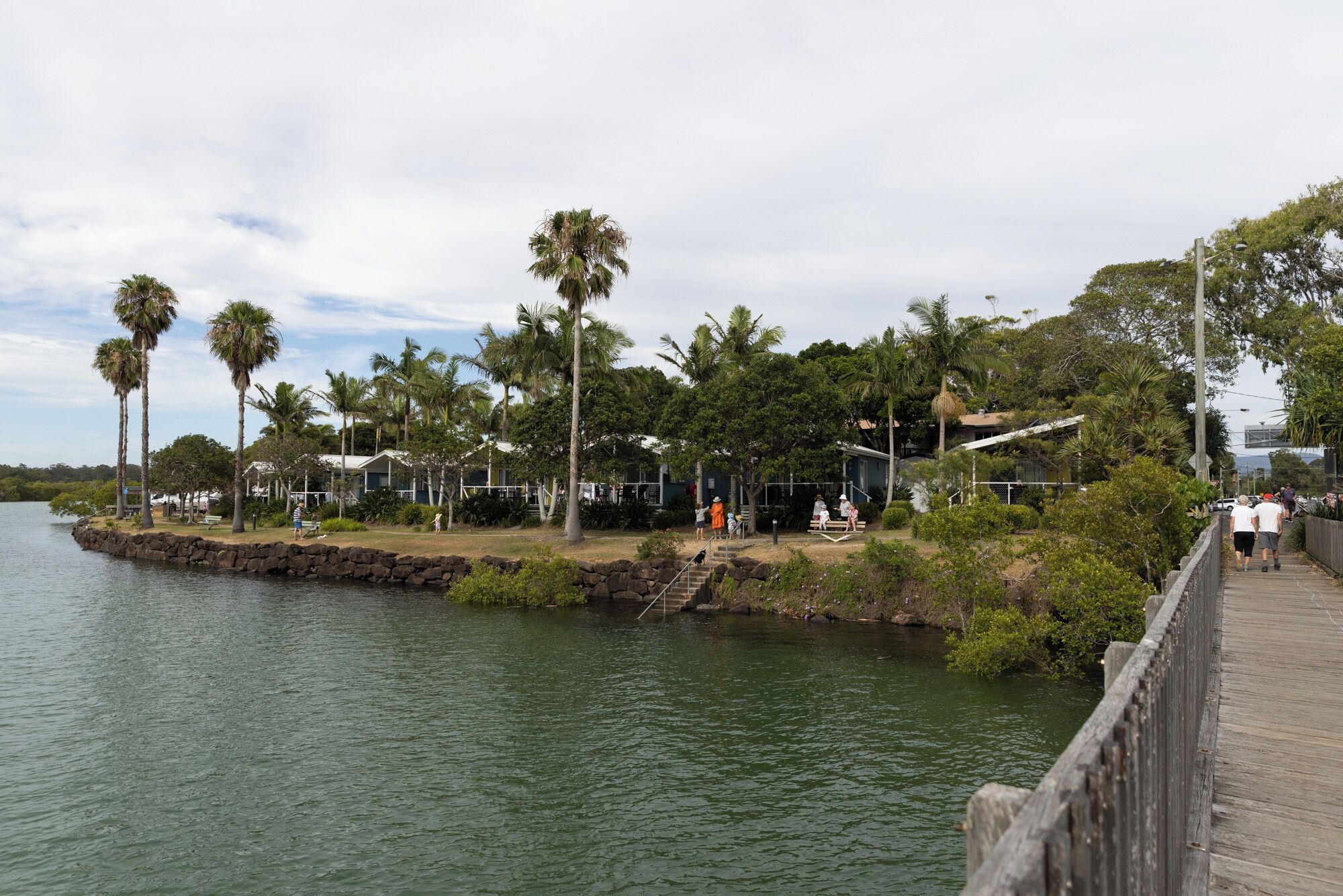 A waterfront property with a wooden deck, palm trees, and a stone wall.