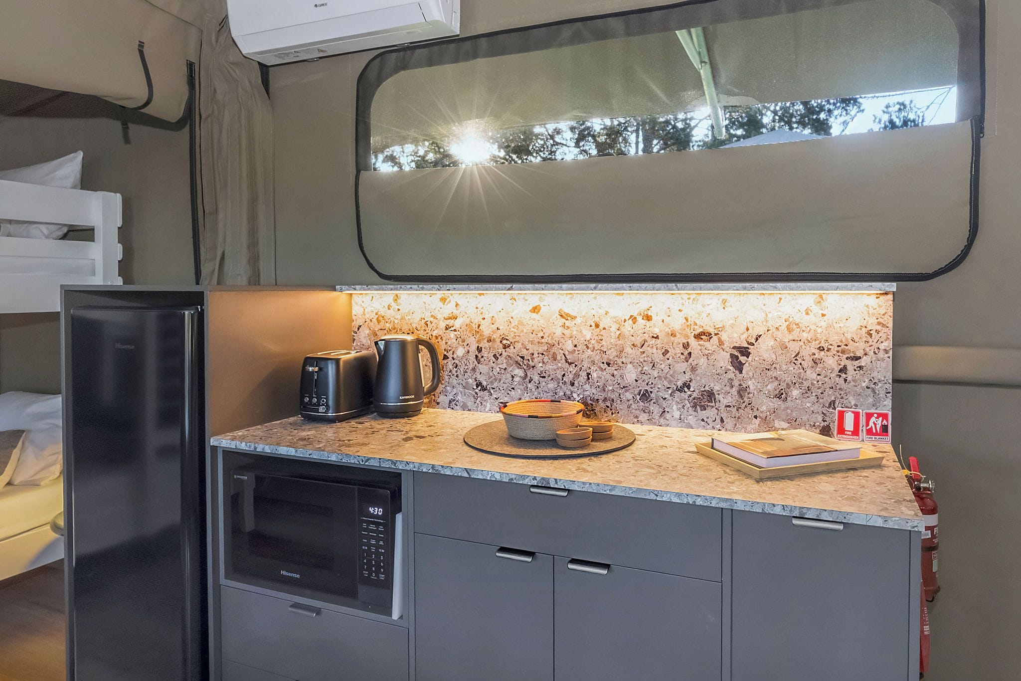 Una kitchenette compacta con microondas, tostadora y cafetera sobre una encimera de granito.