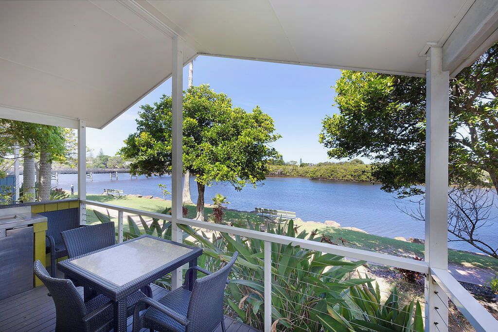 A covered outdoor area with a table and chairs, overlooking a body of water and greenery.
