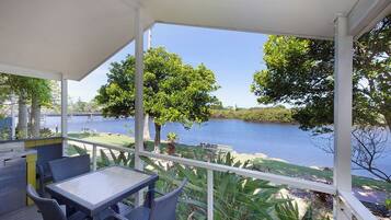 A covered outdoor area with a table and chairs, overlooking a body of water and greenery.