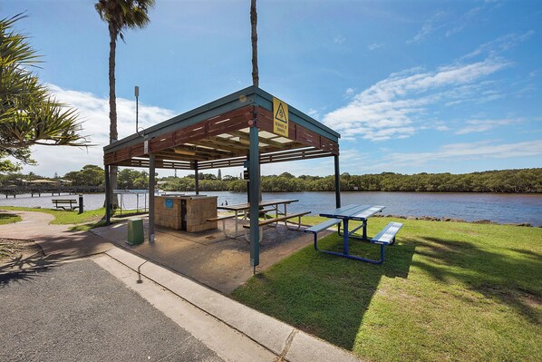 A covered picnic area with benches and a trash bin, overlooking a lake.