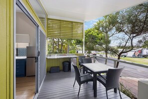 A balcony with a table and chairs, a sliding door leading to a kitchen, and a view of trees and a street. - Reflections Brunswick Head - Holiday Park (Brunswick Heads)